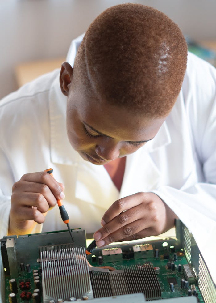 our-story Focused technician in lab coat checking current of electricity with voltmeter while examining condition of graphics card in workshop