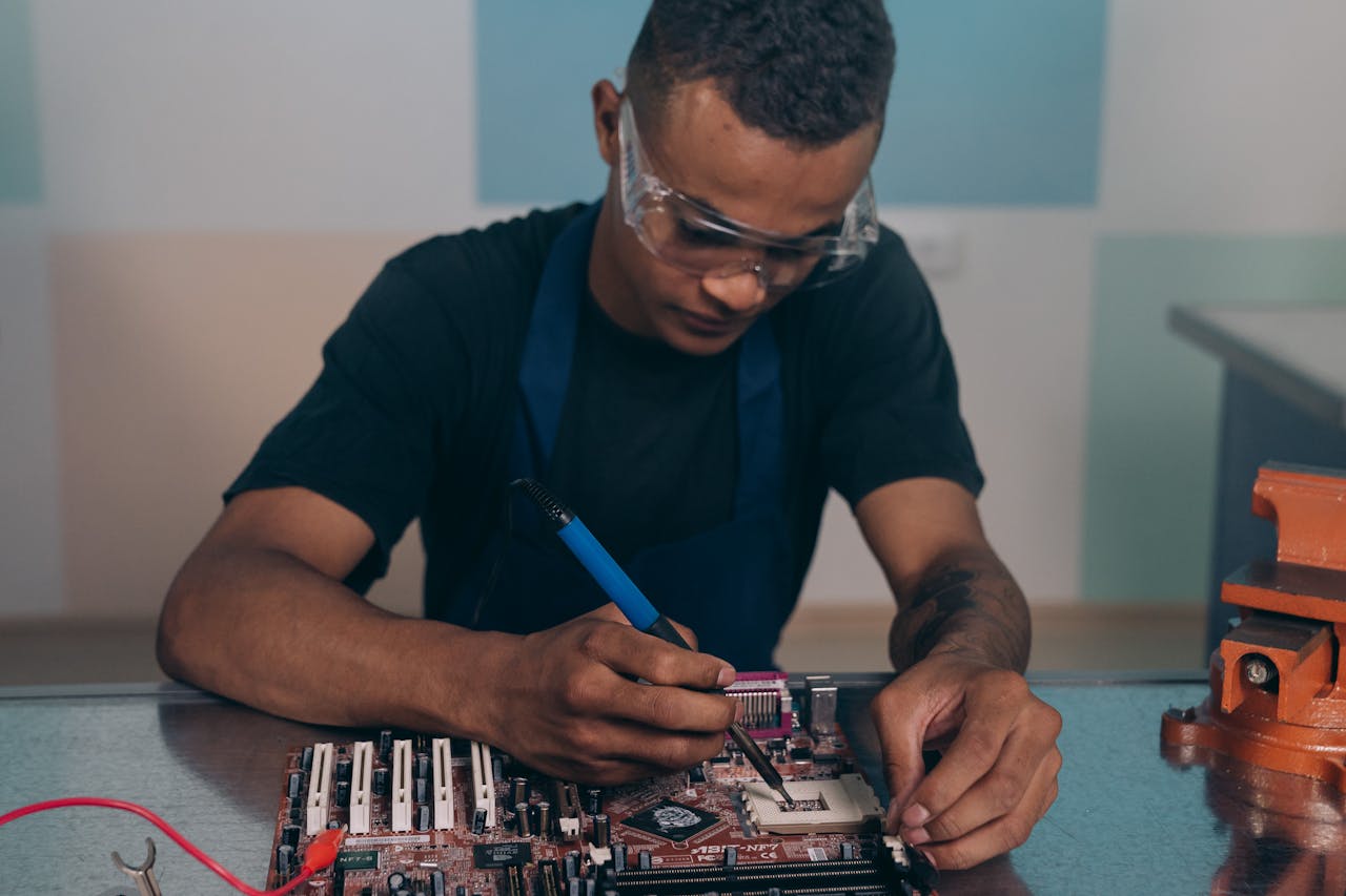 heros-img A technician wearing safety glasses works intently on a computer motherboard with a soldering iron.